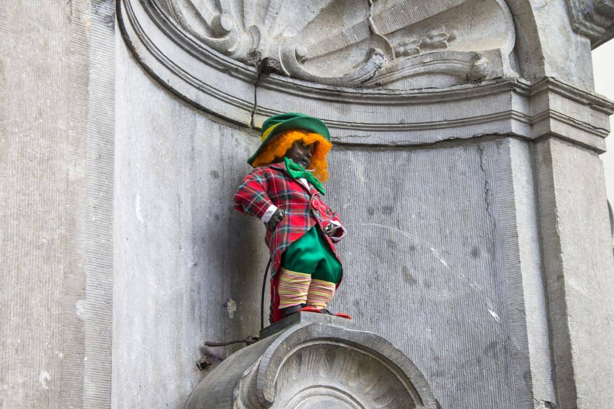 Eine kleine Statue eines Jungen in traditioneller Kleidung mit buntem Hut, die an einer Wand befestigt ist und Wasser spritzt.