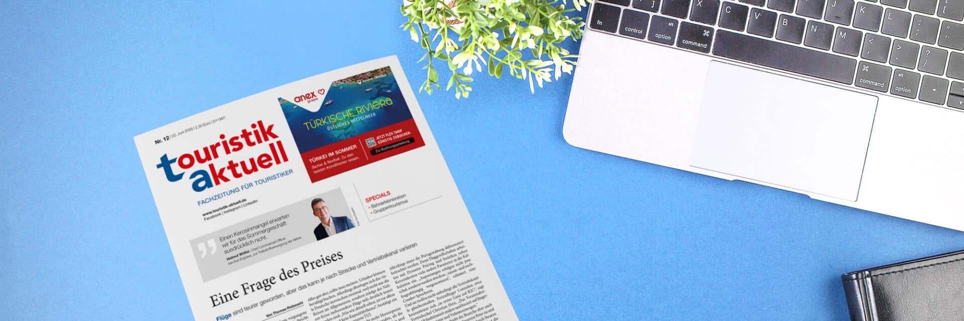 Ein auf einem blauen Tisch liegendes Exemplar der Fachzeitschrift 'touristik aktuell' neben einem Laptop und einer Pflanze.