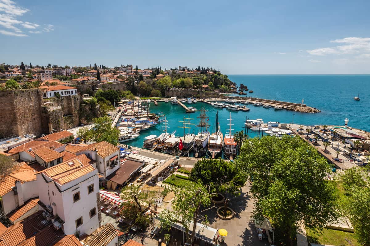 Blick auf den Hafen mit Segelbooten und Yachten, umgeben von mediterraner Vegetation und historischen Gebäuden in Antalya, Türkei.