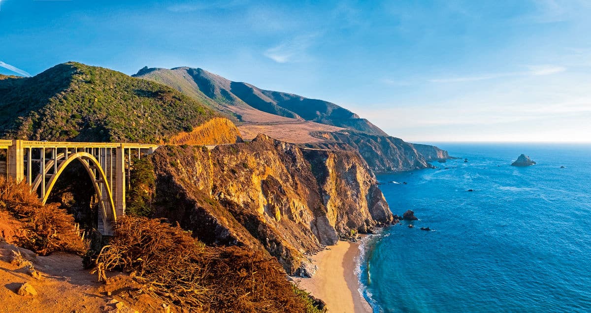 Panoramablick auf die Küste von Big Sur in Kalifornien mit einer Brücke, die über die Klippen führt, und dem ruhigen Ozean im Hintergrund.