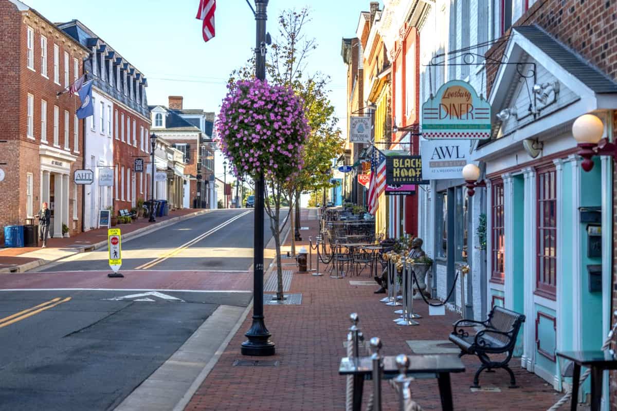 Eine ruhige Straße in einer Kleinstadt in Loudoun County im US-Bundesstaat Virginia, mit historischen Gebäuden, bunten Schildern und blühenden Pflanzen an den Laternen.