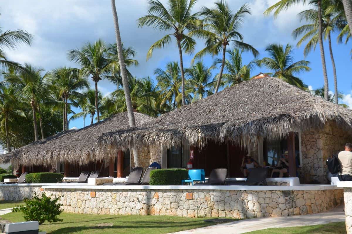 Drei strohgedeckte Bungalows umgeben von Palmen und einem gepflegten Garten, ideal für entspannende Aufenthalte in tropischer Umgebung.