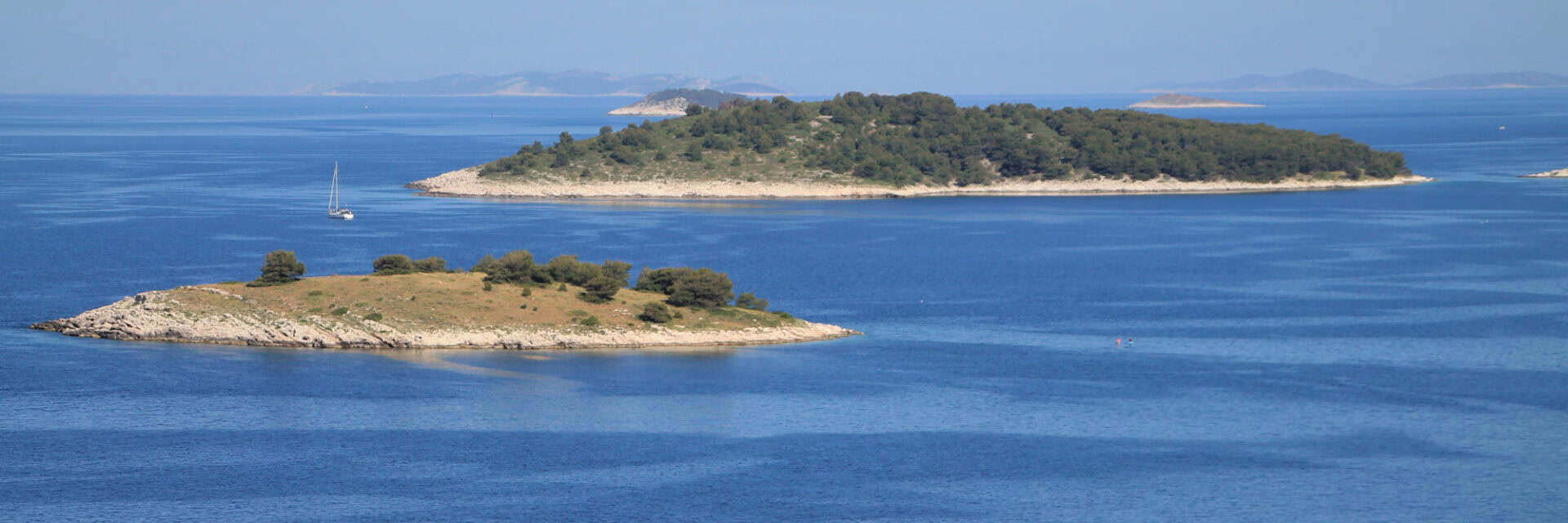 wm-serie-kroatien2 Blick auf mehrere kleine Inseln im blauen Wasser, umgeben von sanften Hügeln und einer klaren Himmel, ideal für maritime Erkundungen.
