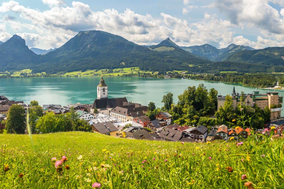 wolfgangsee st. wolfgang Panoramablick auf eine malerische Stadt am Ufer eines Sees, umgeben von grünen Wiesen und Bergen unter einem blauen Himmel mit Wolken.