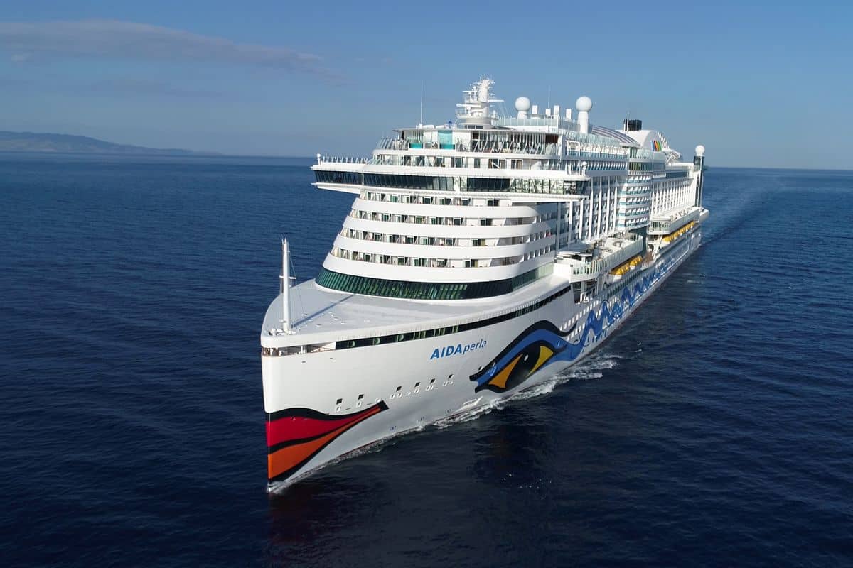 Die Aida Perla fährt auf ruhigem, blauem Meer. Das Kreuzfahrtschiff ist von vorne rechts zu sehen und zeigt den charakteristischen Kussmund am Bug.