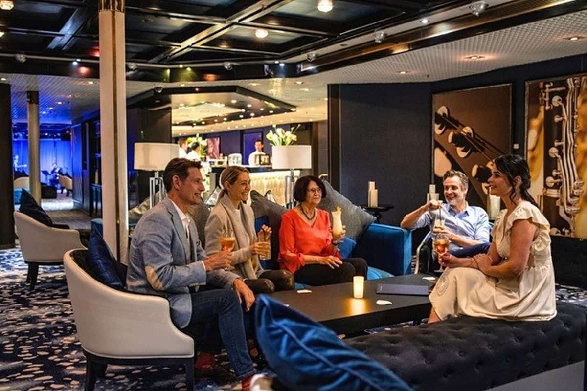 Eine Gruppe von fünf Personen sitzt in einer eleganten Lounge, umgeben von stilvollen Möbeln und sanfter Beleuchtung, während sie Getränke genießen.