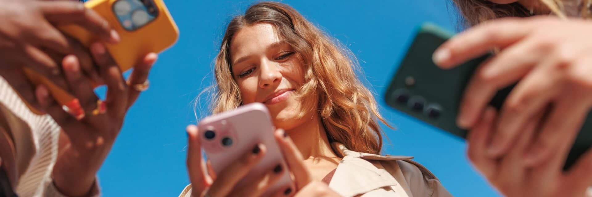 Eine Gruppe von Personen, die ihre Smartphones in der Hand halten, während sie nach oben schauen. Der Himmel ist klar und blau.