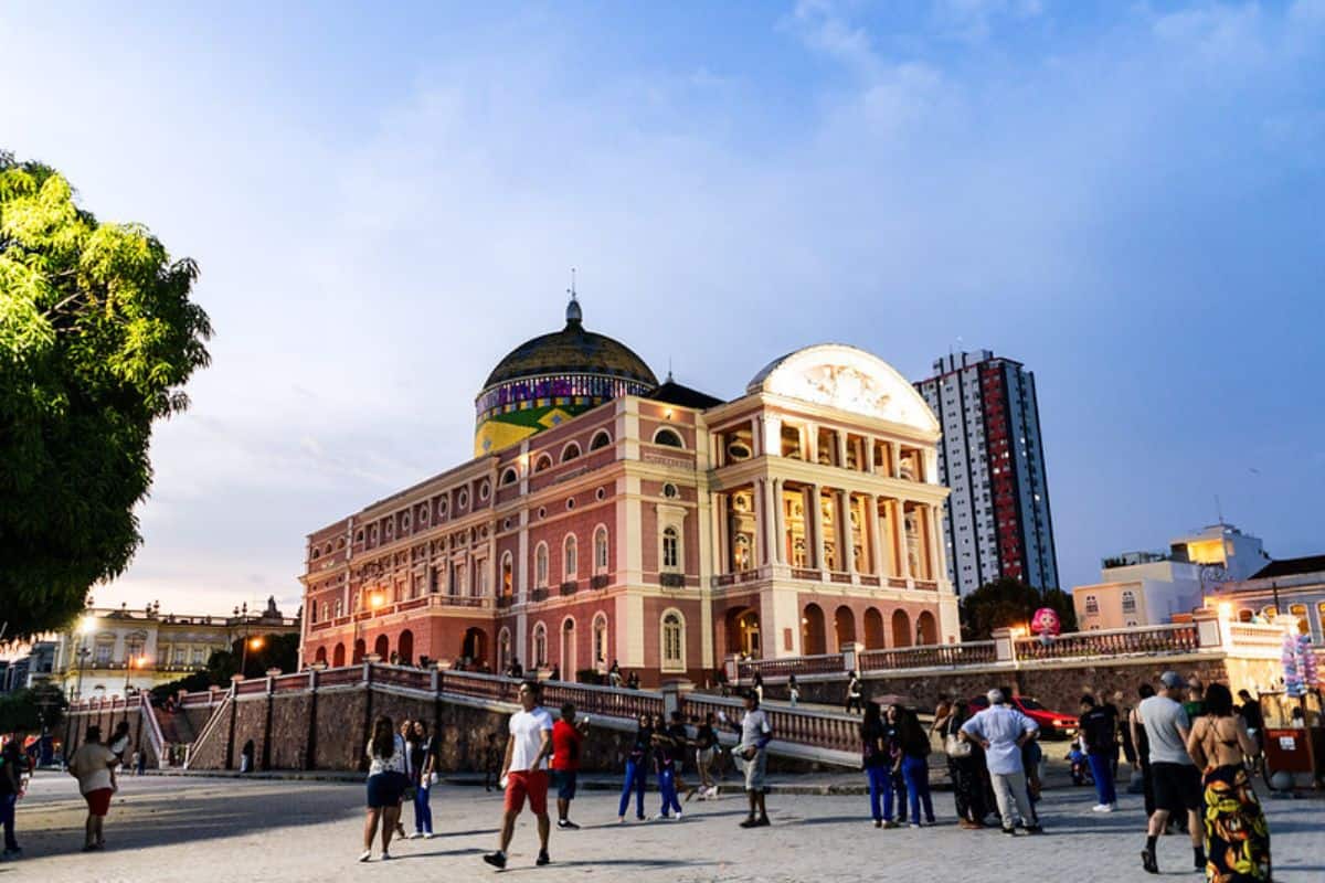 Das historische Teatro Amazonas in Manaus mit seiner markanten rosa Fassade und der bunten Kuppel bei Tageslicht, umgeben von Menschen auf einem Vorplatz.