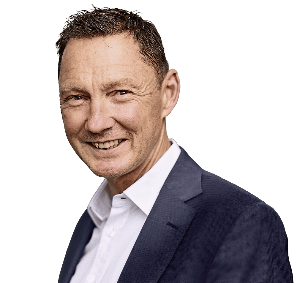 Ein Mann mit kurzem, dunklem Haar und freundlichem Lächeln trägt ein weißes Hemd unter einem dunkelblauen Sakko vor einem neutralen, hellen Hintergrund.