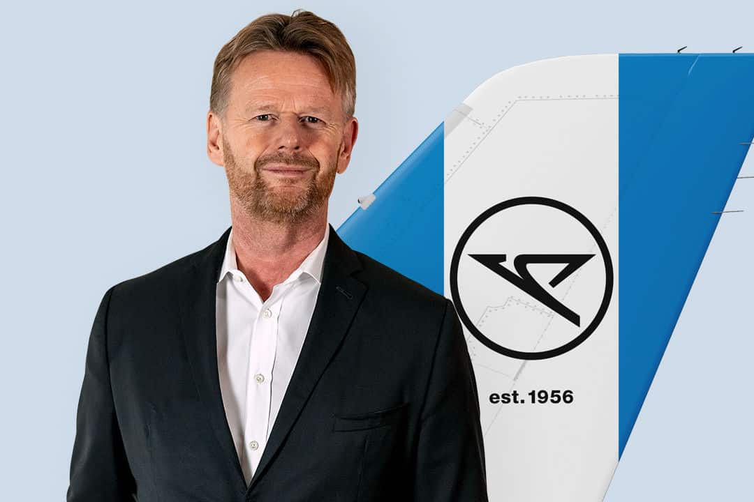 Ein Manager im weißen Hemd und schwarzen Jackett steht vor einer Heckflosse der Airline Condor mit Logo.
