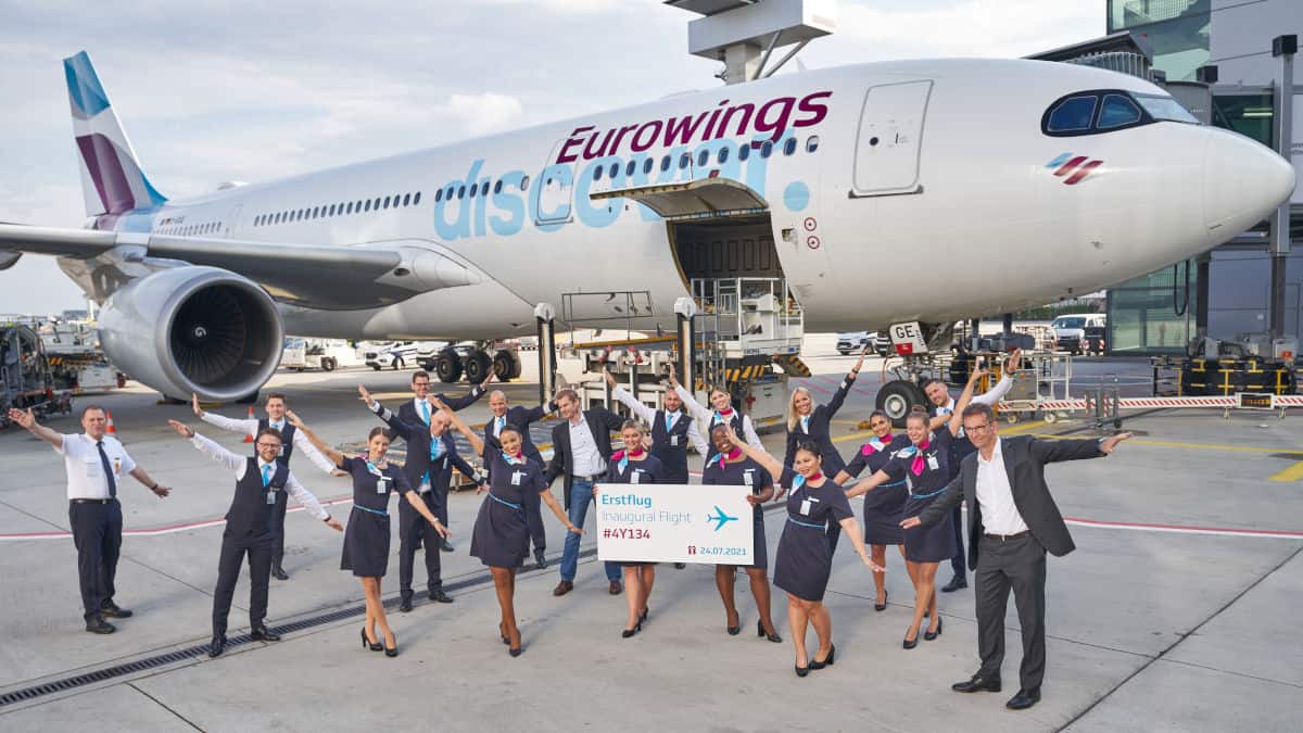 Eine Gruppe von Flugpersonal und Mitarbeitern posiert vor einem Eurowings Discover Flugzeug auf dem Rollfeld, in der Mitte wird ein Schild hochgehalten.