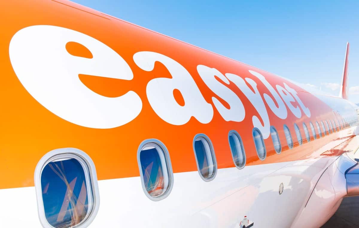 Nahaufnahme eines Flugzeugs der Airline Easyjet mit orangefarbenem Oberteil und großen weißen Buchstaben, die den Namen der Fluggesellschaft zeigen, unter blauem Himmel.