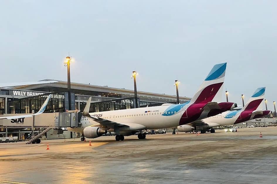 Zwei Flugzeuge der Fluggesellschaft Eurowings stehen am Flughafen Berlin Brandenburg vor dem Terminalgebäude Willy Brandt bei bewölktem Tageslicht.