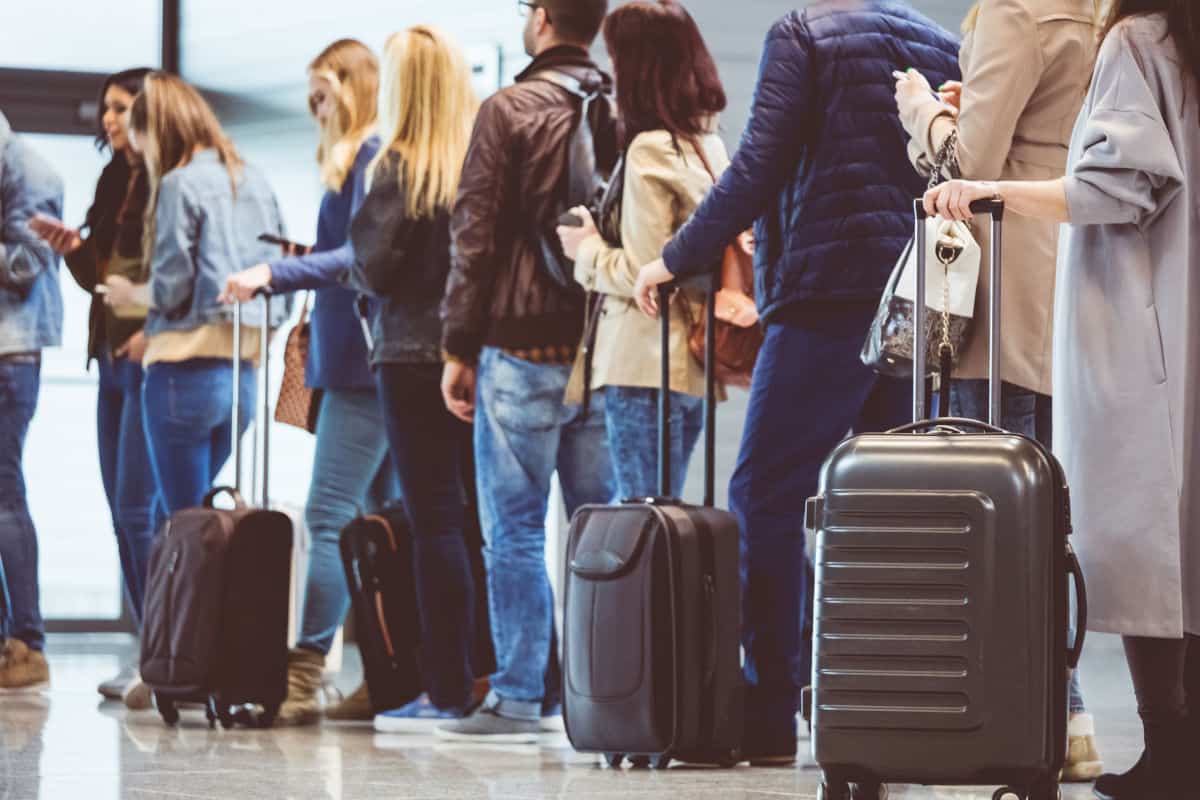 Eine Gruppe von Reisenden steht in einer Schlange am Flughafen, während sie Gepäckstücke mit sich führen und auf den Check-in warten.
