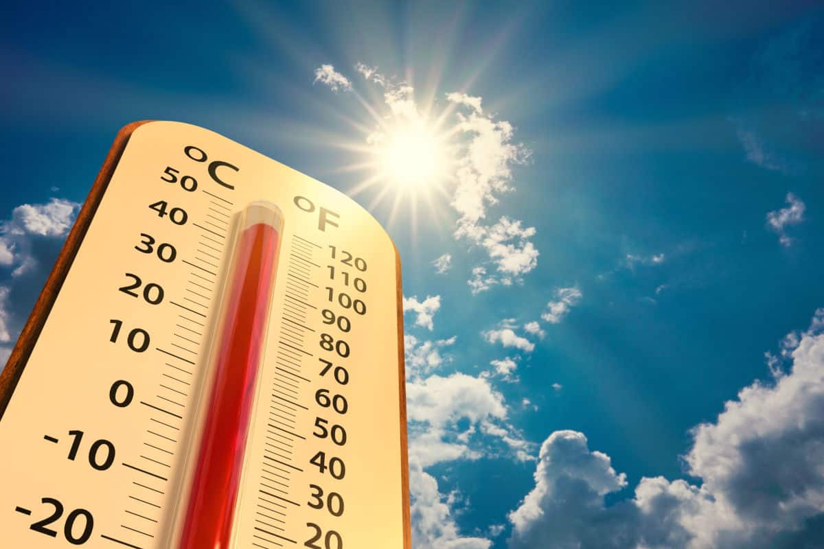 Ein Thermometer mit Celsius- und Fahrenheit-Skala vor einem strahlend blauen Himmel mit hellem Sonnenschein und vereinzelten weißen Wolken im Hintergrund.