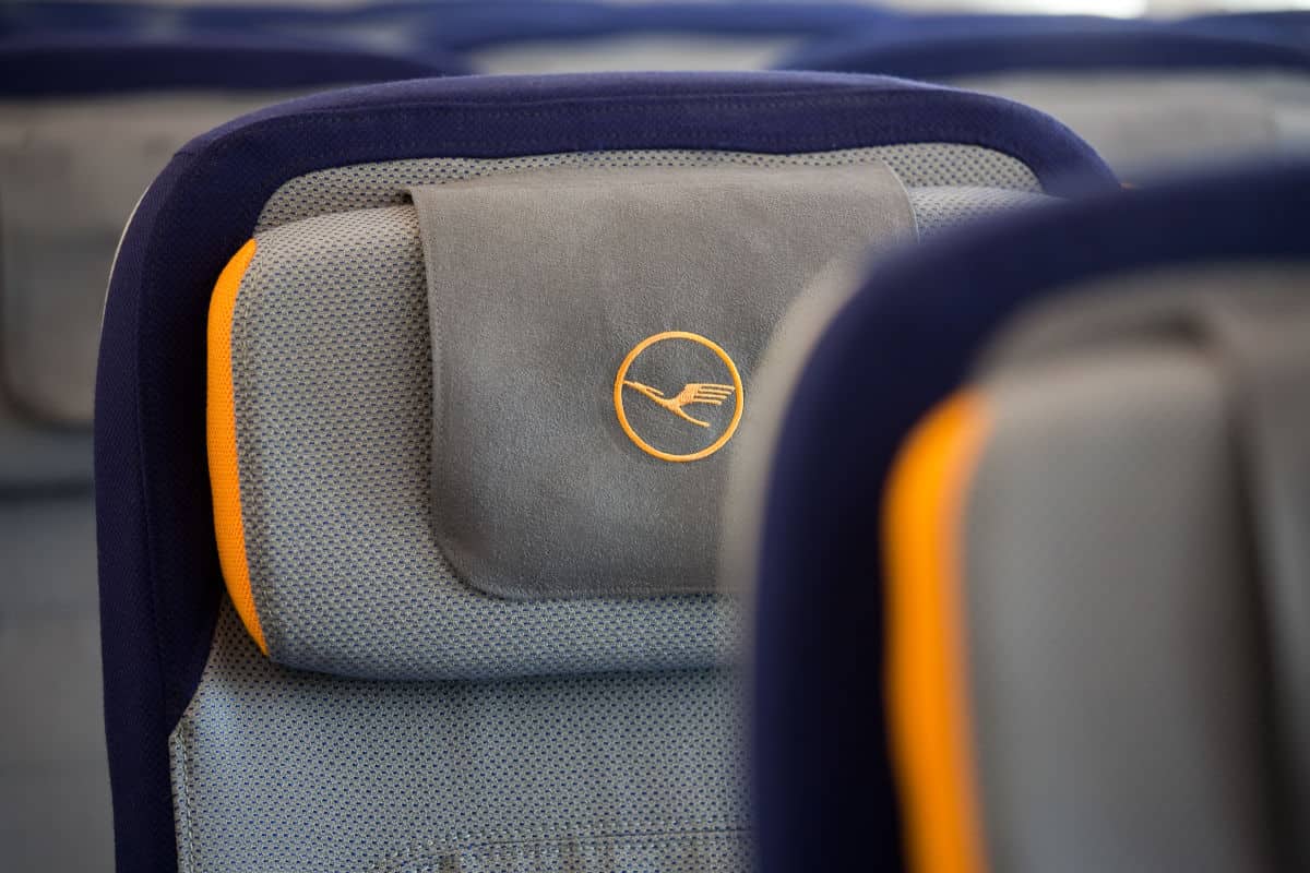 Nahaufnahme eines grauen Kopfstützenbezugs mit dem Logo von Lufthansa auf einem Flugzeugsitz.