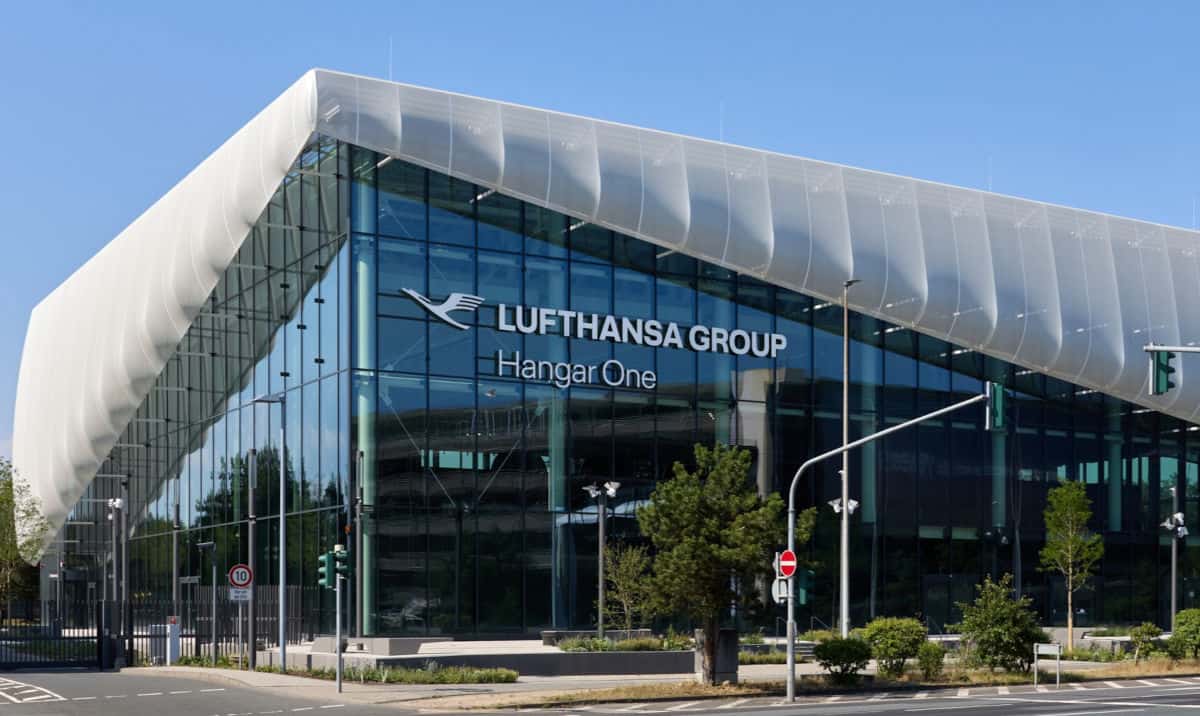 Die moderne Glasfassade des Hangar One der Lufthansa Group mit markantem, weißem Membrandach vor einem klaren blauen Himmel an einem sonnigen Tag.