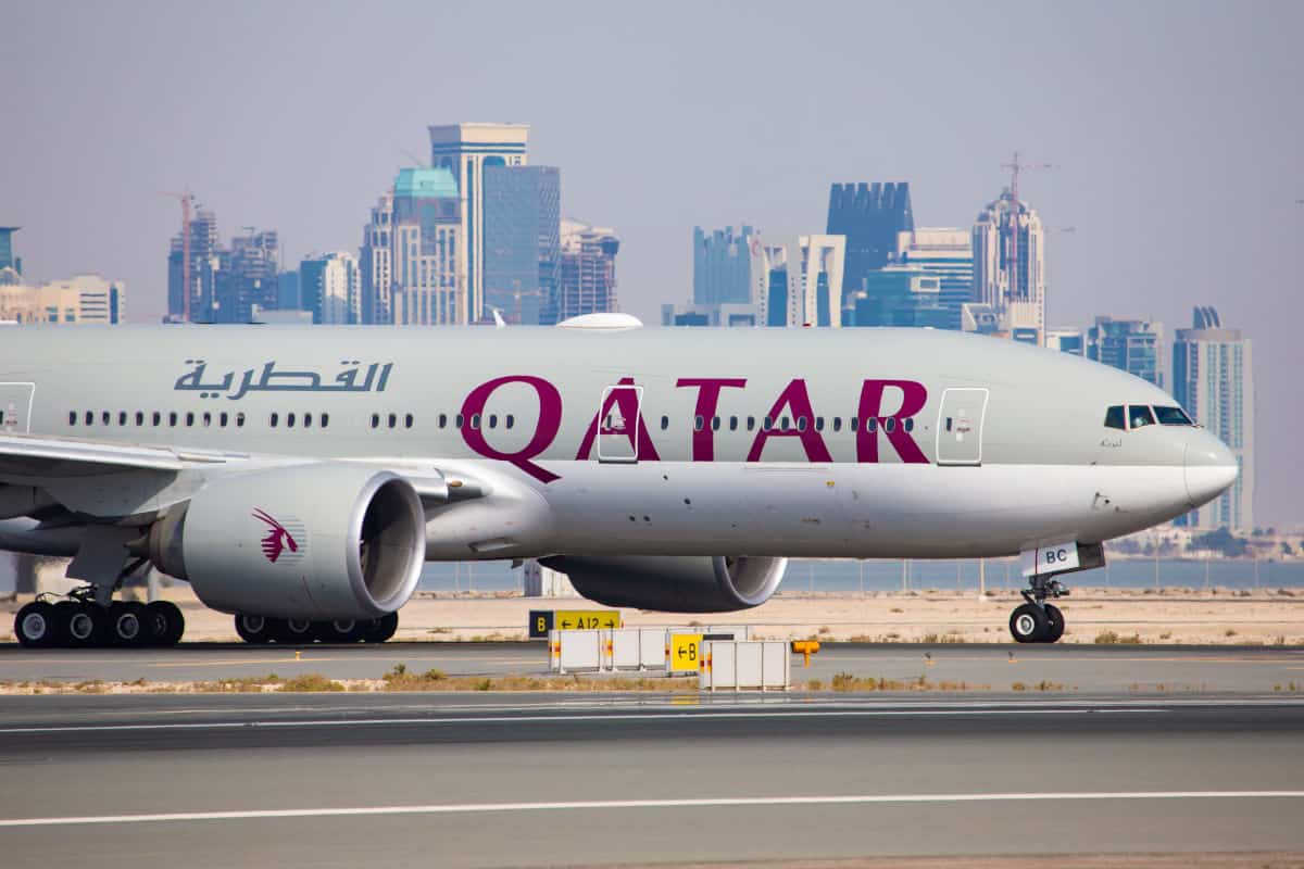Ein Qatar Airways Flugzeug auf dem Rollfeld mit einer modernen Stadtlandschaft im Hintergrund, die Wolkenkratzer und Bauarbeiten zeigt.
