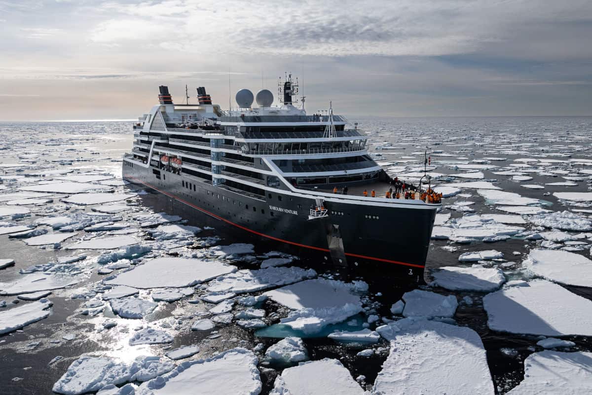 Die Seabourn Venture fährt durch ein Eismeer mit zahlreichen treibenden Eisschollen unter einem bewölkten Himmel in einer arktischen Umgebung.