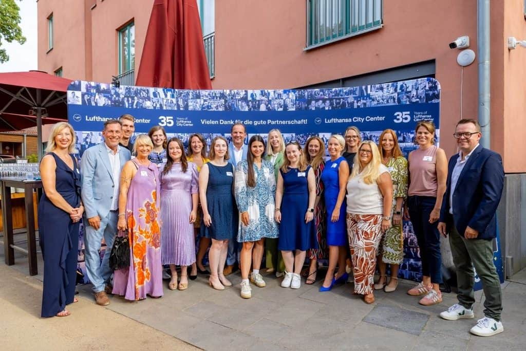 Eine Gruppe von 17 Personen posiert vor einer großen Fotowand von Lufthansa City Center mit der Aufschrift 35 Jahre und Dank für die gute Partnerschaft.