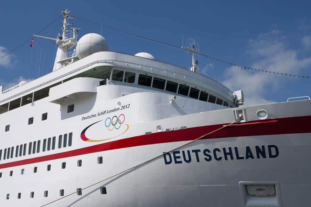 Nahaufnahme des weißen Kreuzfahrtschiffs Deutschland mit dem Schriftzug Deutsches Schiff London 2012 und den olympischen Ringen vor einem blauen Himmel.