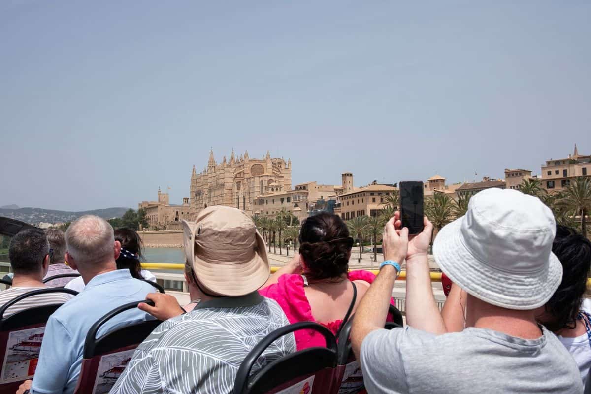 Blick von einem offenen Sightseeing-Bus auf die Kathedrale von Palma de Mallorca, während mehrere Personen in der vorderen Reihe Fotos mit Handys machen.
