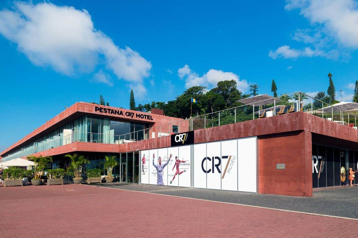 Das Pestana CR7 Hotel mit dem angrenzenden CR7 Museu in einem modernen, rötlichen Gebäude unter blauem Himmel mit Pflanzen und einer Dachterrasse.