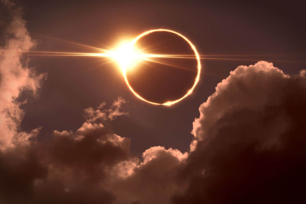 Eine ringförmige Sonnenfinsternis am dunklen Himmel, bei der ein heller Lichtring hinter dunklen, teilweise beleuchteten Wolkenformationen zu sehen ist.