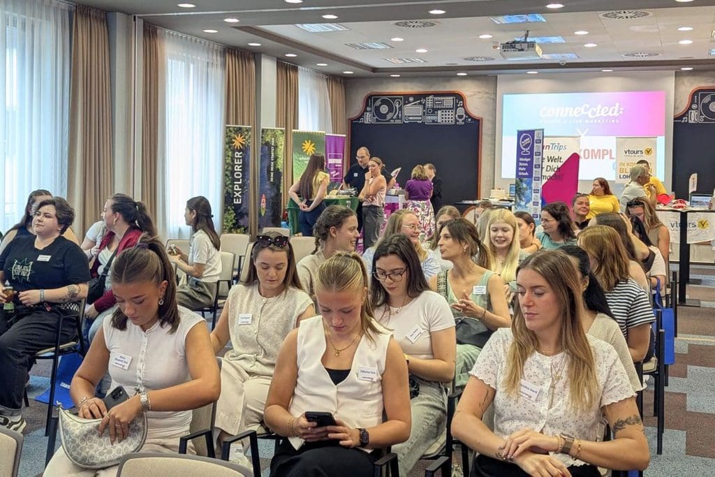 Ein Publikum aus überwiegend jungen Frauen sitzt in einem hellen Konferenzraum auf Stühlen und blickt aufmerksam nach vorne oder auf ihre Smartphones.