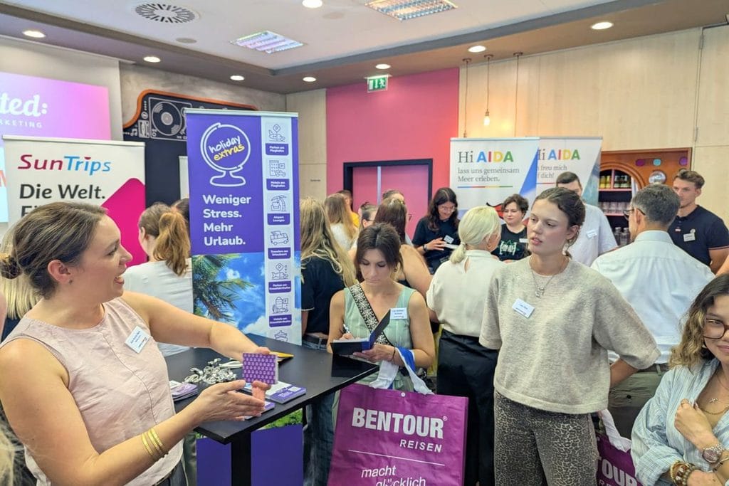 Eine Frau präsentiert an einem Messestand Informationsmaterial, während im Hintergrund weitere Personen vor Roll-up-Displays von Holiday Extras stehen.