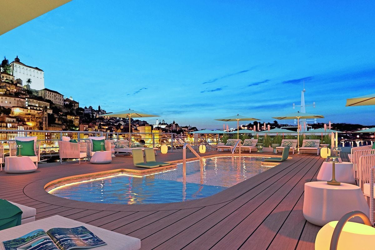 Ein beleuchteter Pool auf einem Schiffsdeck bei Dämmerung mit Liegestühlen und Sonnenschirmen vor einer nächtlichen Stadtkulisse am Hang mit vielen Lichtern.