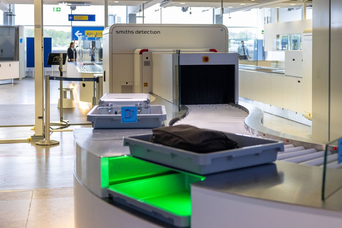 Eine Sicherheitskontrollstelle am Flughafen mit einem Röntgengerät von Smiths Detection, Förderbändern und grauen Kunststoffwannen für das Handgepäck.