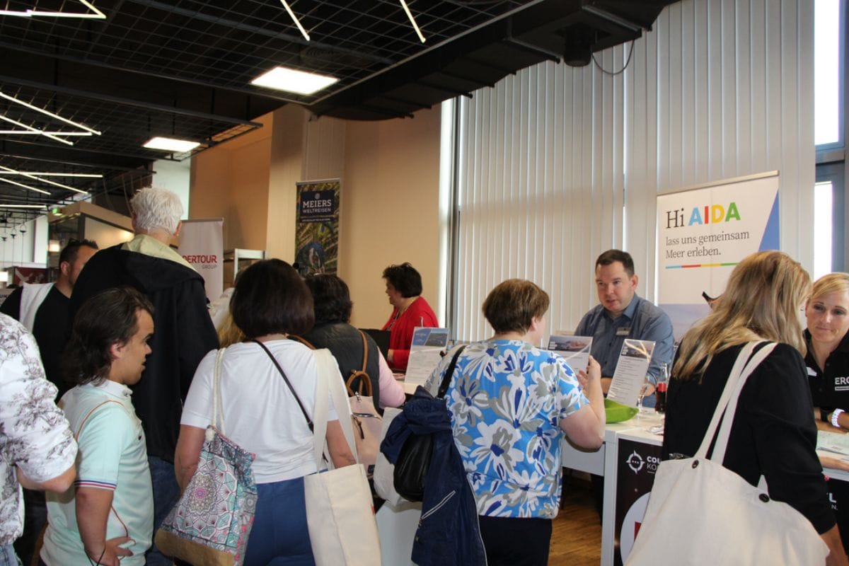 Mehrere Personen stehen an einem Messestand von AIDA und führen Gespräche mit dem Personal, im Hintergrund sind weitere Firmenbanner und Besucher zu sehen.