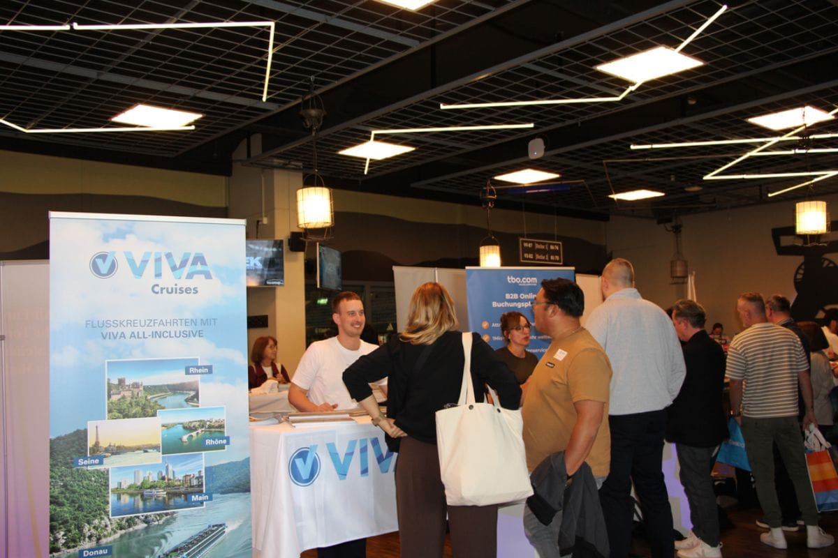 Ein Messestand von VIVA Cruises in einer Halle mit Gitterdecke, an dem ein Mitarbeiter hinter einem Tisch mit Besuchern im Gespräch steht. Weitere Personen.