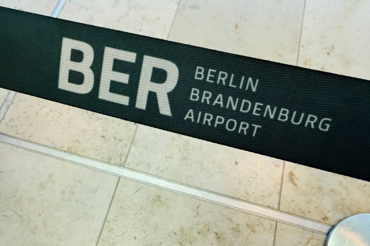 Ein schwarzes Absperrband mit dem weißen Aufdruck BER Berlin Brandenburg Airport vor einem hellen, gefliesten Boden in einem Flughafenbereich.