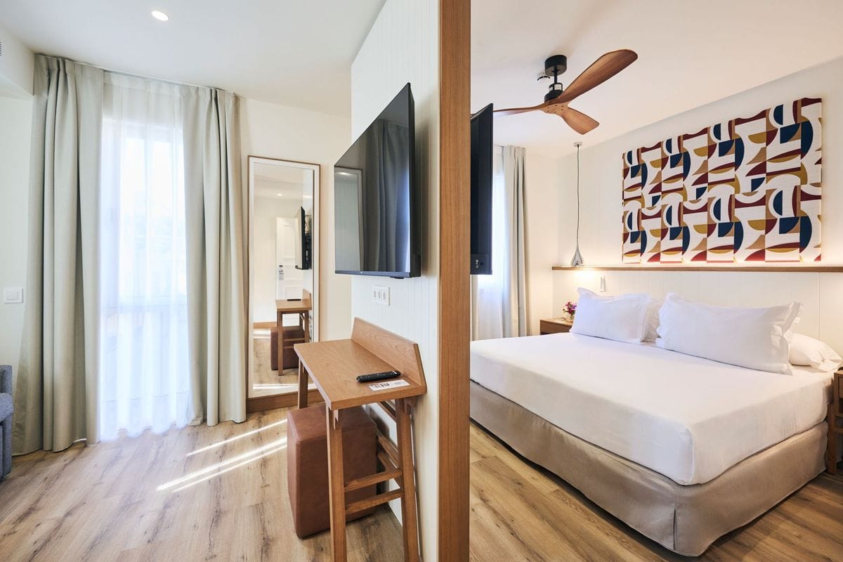 Ein modernes Hotelzimmer mit einem Doppelbett, einem Fernseher, einem Schreibtisch und einem großen Fenster mit Vorhängen.