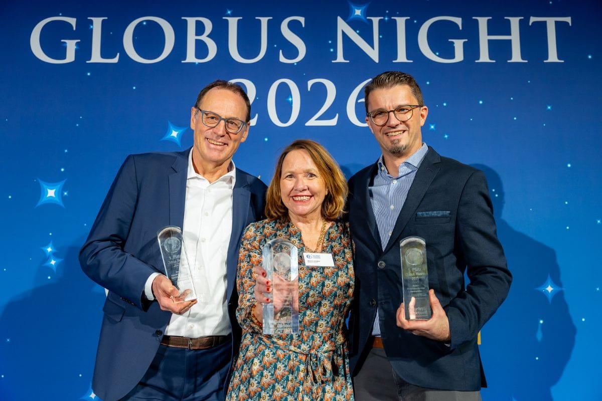 Zwei Männer in Anzügen und eine Frau in einem gemusterten Kleid stehen vor einer blauen Wand mit der Aufschrift Globus Night 2020 und halten Trophäen.