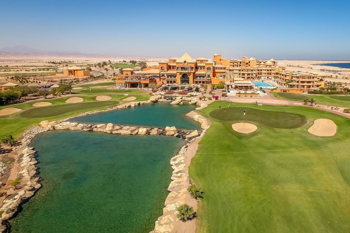 Luftaufnahme eines Golfplatzes mit einem Hotel, Wasserflächen und Wüstenlandschaft im Hintergrund.
