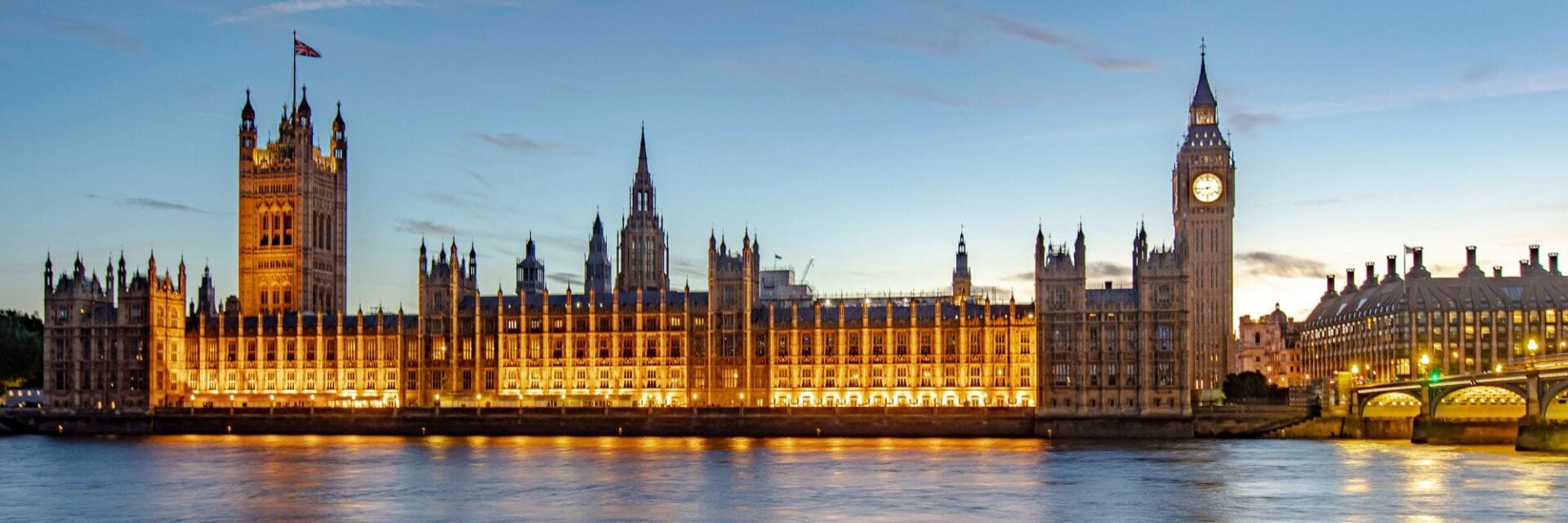 london Die beleuchteten Houses of Parliament mit dem Elizabeth Tower und Big Ben in London bei Dämmerung, gesehen vom Ufer der Themse aus in einer Totalen.