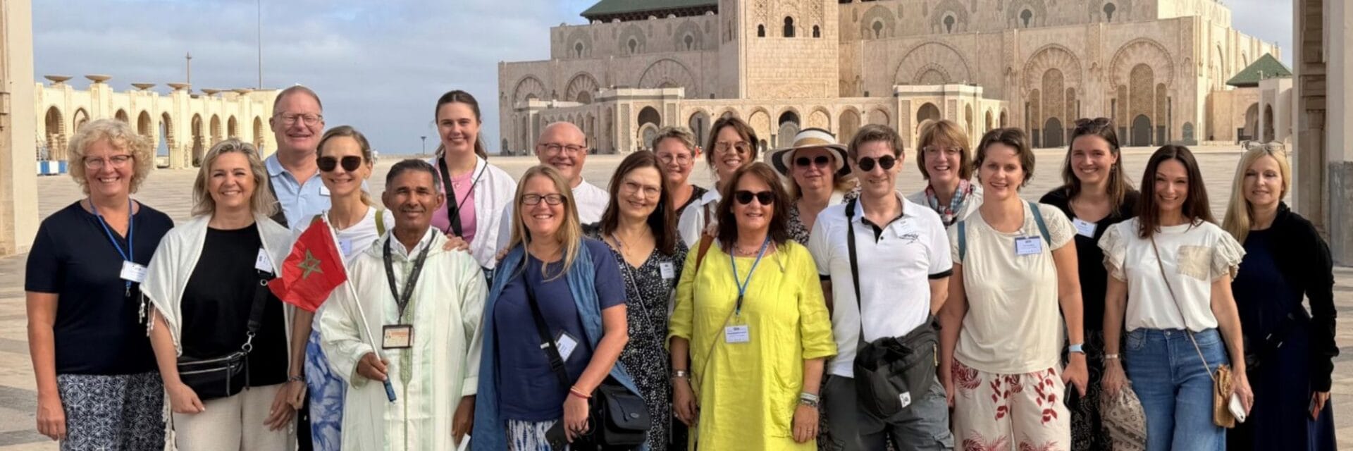 trendtours-fam-trip Eine Gruppe von Menschen posiert vor der Hassan-II.-Moschee in Casablanca. Eine Person hält eine kleine marokkanische Flagge in der Hand, alle lächeln.