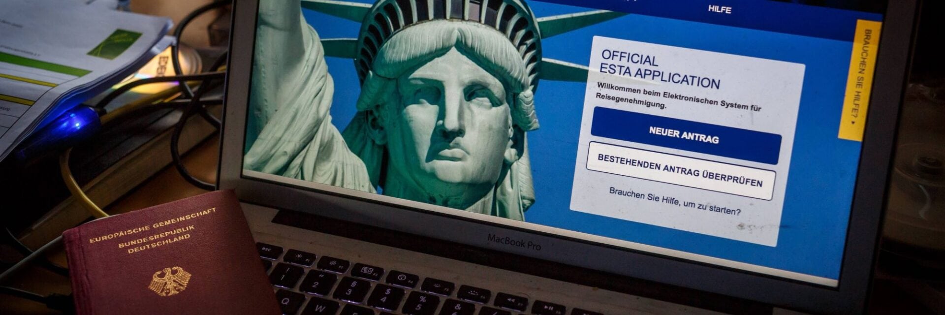 usa-reisepass-esta Ein Laptop-Bildschirm zeigt die offizielle ESTA-Webseite mit der Freiheitsstatue, daneben liegt ein Reisepass der Bundesrepublik Deutschland auf dem Tisch.