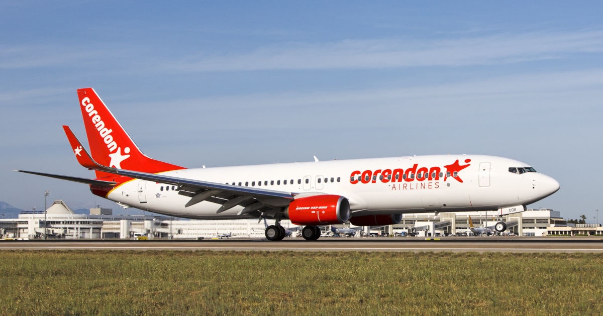 Ein Flugzeug der Corendon Airlines steht auf dem Rollfeld, umgeben von einem Flughafen mit Gebäuden im Hintergrund.