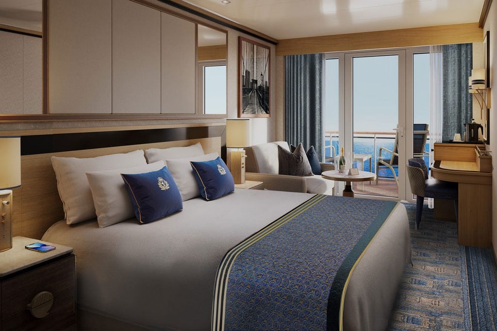 Eine moderne Kreuzfahrtschiff-Kabine mit einem Doppelbett, blauen Zierkissen, einem kleinen Sitzbereich und einem Balkon mit Blick auf das offene Meer.