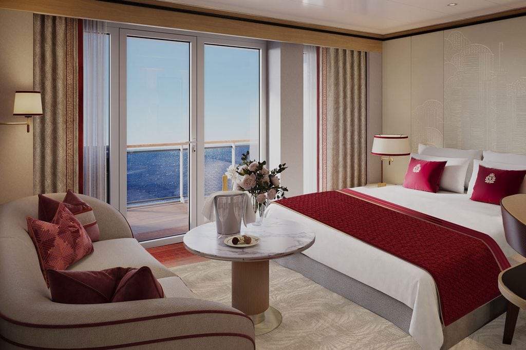 Eine luxuriöse Schiffskabine mit Doppelbett, rotem Bettläufer, geschwungenem Sofa, Marmortisch mit Sektkühler und einem Balkon mit Blick auf das blaue Meer.
