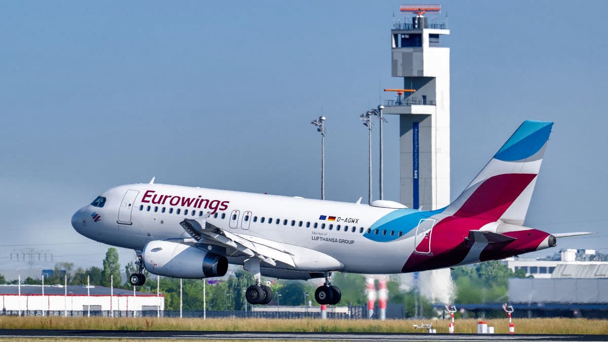 Ein Eurowings-Flugzeug landet auf einer Startbahn, im Hintergrund ist ein Kontrollturm zu sehen.