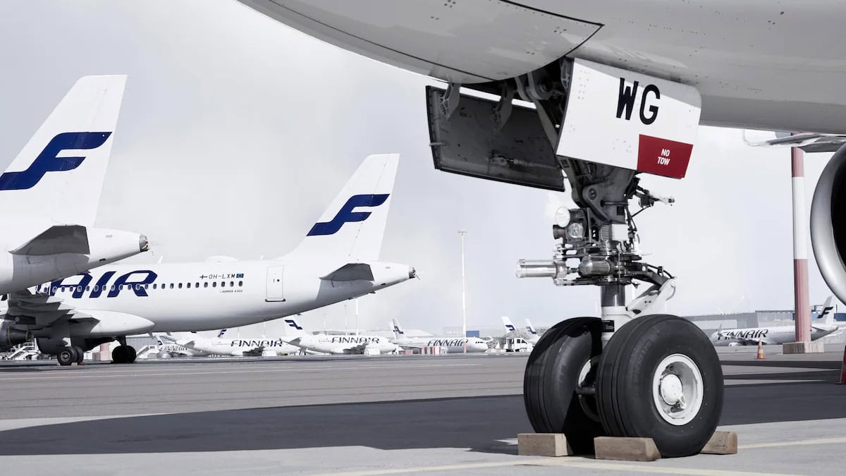 Nahaufnahme eines Flugzeugfahrwerks im Vordergrund, dahinter stehen mehrere Flugzeuge der Fluggesellschaft Finnair auf dem Rollfeld eines Flughafens.