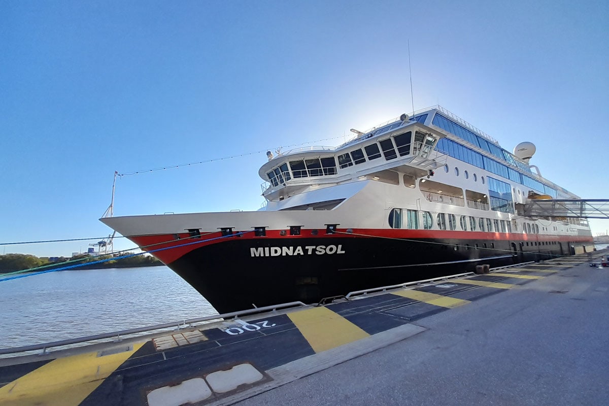 Das Kreuzfahrtschiff Midnatsol liegt an einem Kai festgemacht im Hafen. Der Rumpf ist schwarz und rot lackiert, im Hintergrund ist ein klarer blauer Himmel.