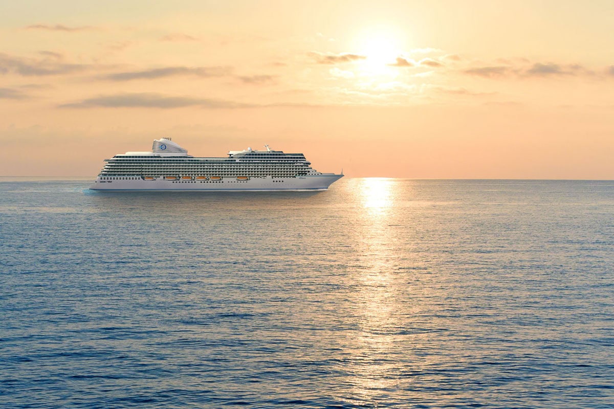 Ein weißes Kreuzfahrtschiff fährt bei Sonnenuntergang auf dem ruhigen Meer, wobei sich das goldene Licht der Sonne auf der Wasseroberfläche spiegelt.