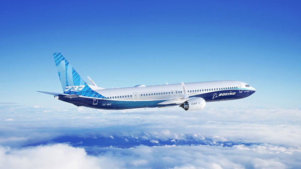 Ein Boeing 737 MAX Flugzeug fliegt hoch über den Wolken vor einem klaren blauen Himmel.