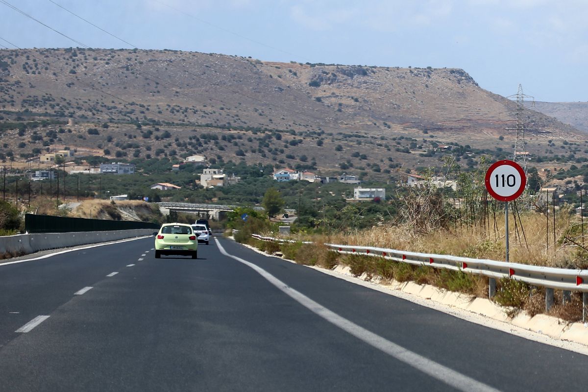 Eine asphaltierte Landstraße führt durch eine hügelige Landschaft, rechts steht ein Verkehrsschild mit der Geschwindigkeitsbegrenzung von 110 Stundenkilometern.